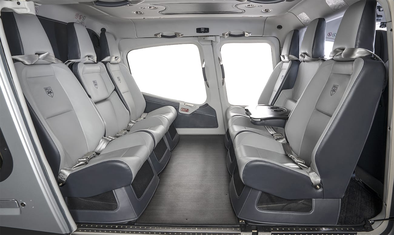 Interior of a helicopter featuring six grey leather seats arranged in two rows with large windows.