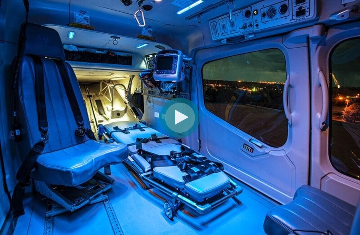 Interior of a medical helicopter, featuring blue lighting, seats, and a stretcher area.