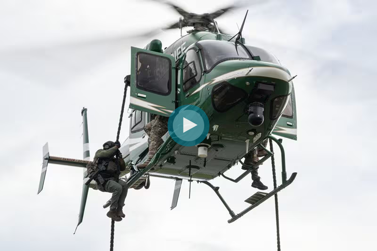 A helicopter hovers with soldiers rappelling down from the side, securing a tactical operation.
