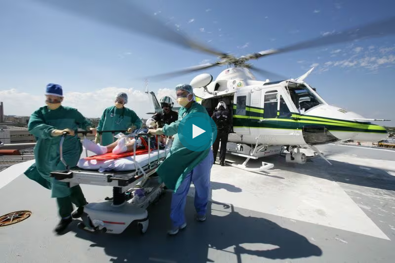 Medical staff transporting a patient on a stretcher to a helicopter for airlift on a rooftop.