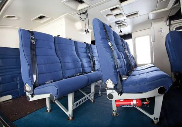 Interior of a helicopter featuring blue passenger seats with seatbelts, arranged in two rows.