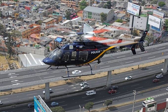 A police helicopter hovers above a busy highway in an urban area with buildings and billboards.