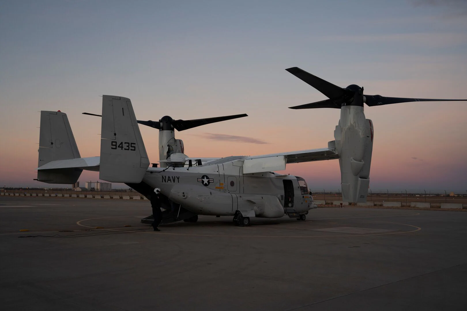 Osprey tiltrotor aircraft on a runway with a sunset backdrop.