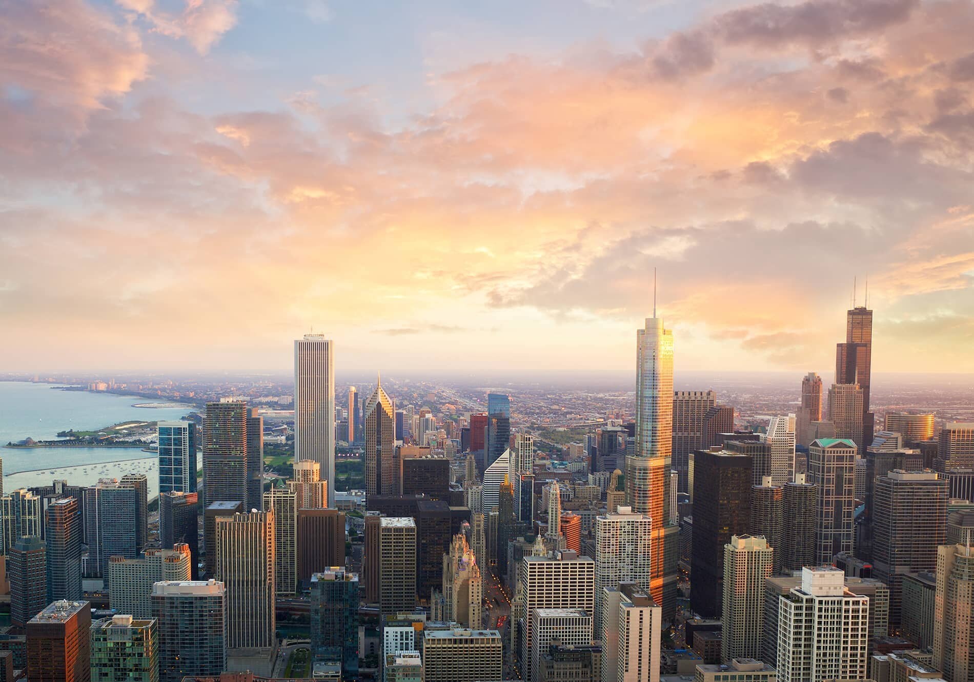 Aerial view of a city skyline at sunset, featuring tall skyscrapers and a waterfront. Cloudy sky.