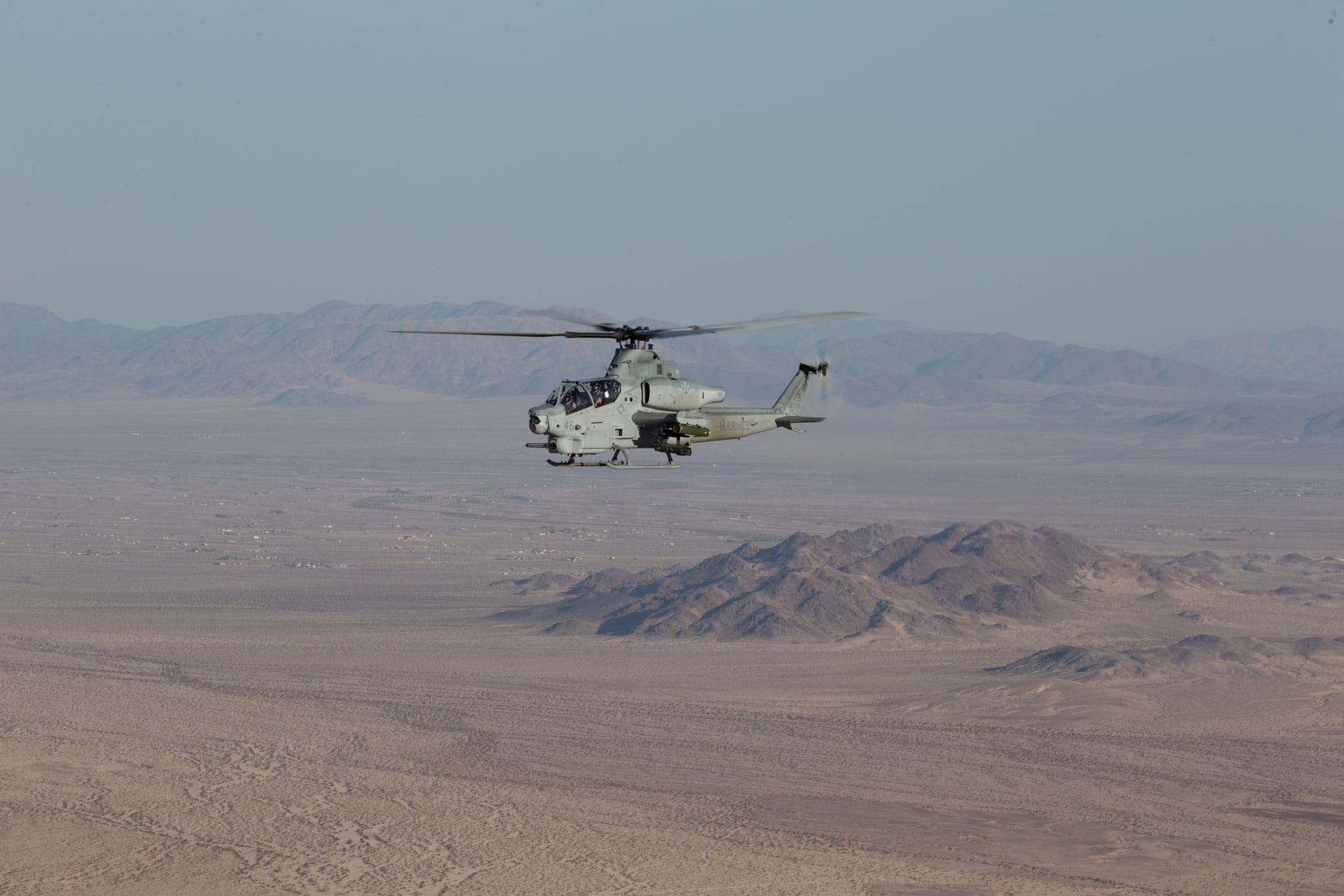 A military helicopter flying over a desert landscape with mountains in the background.
