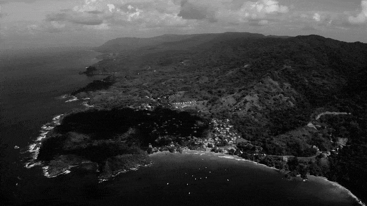 Aerial view of a coastal area with mountains and a small village near the shore.