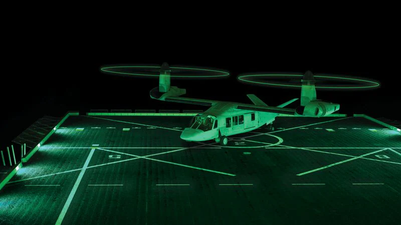 An illuminated tiltrotor aircraft on a helipad, surrounded by green lighting at night.