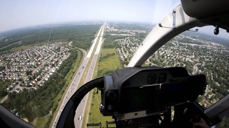 Aerial view from a helicopter cockpit showing a highway and suburban neighborhoods.
