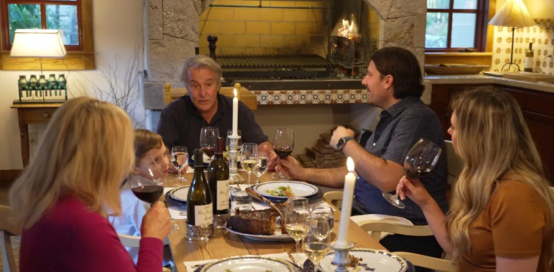 A family dinner scene with five people enjoying a meal, wine, and a cozy fireplace in the