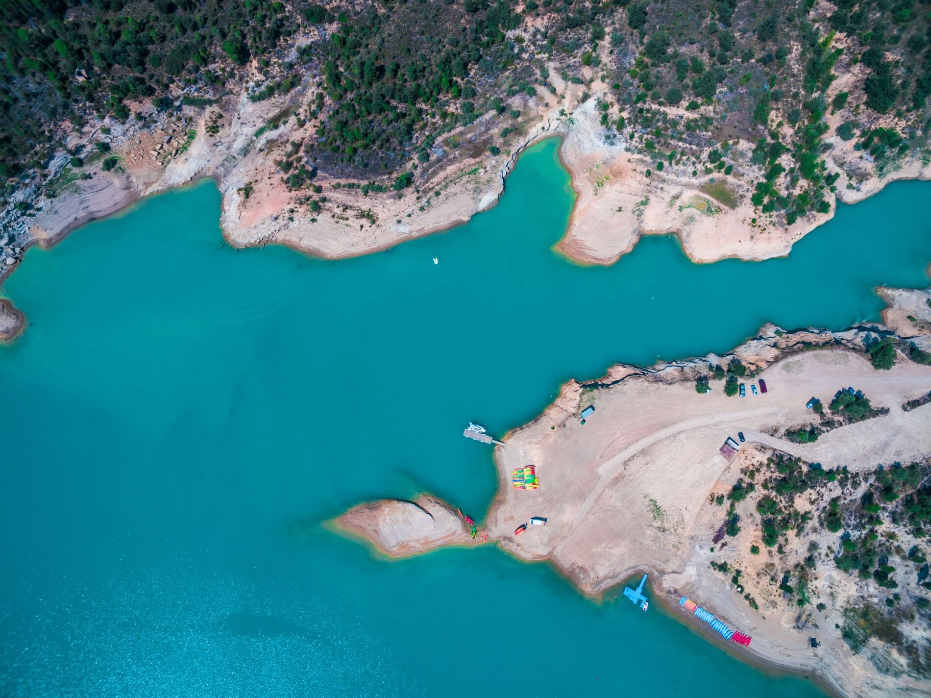 Aerial view of a turquoise lake surrounded by sandy shores and greenery. Boats and beach areas