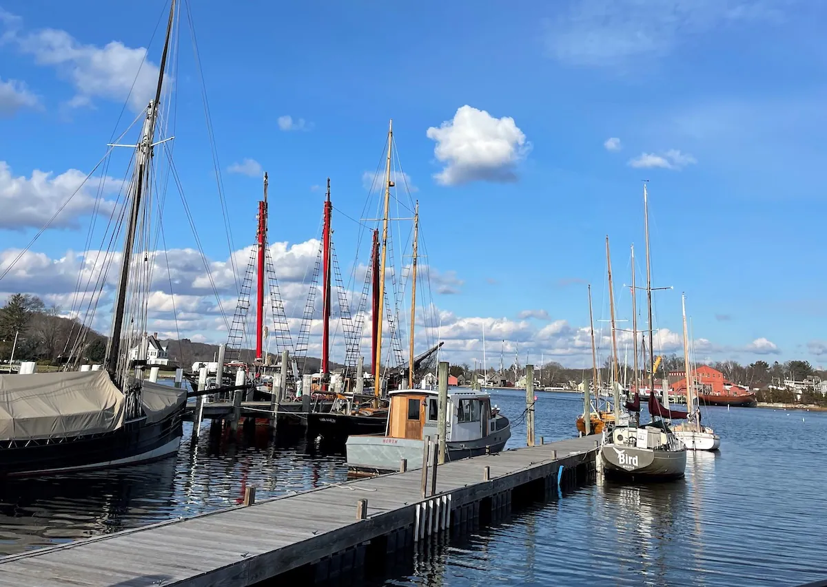 Dock with several boats moored, under a blue sky with fluffy clouds and calm water.