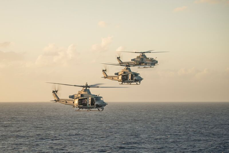 Three military helicopters flying in formation over the ocean during sunset.