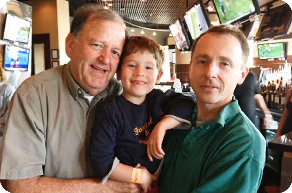 Three generations of men in the Siff family smiling and posing together in a bar with TVs in the background.