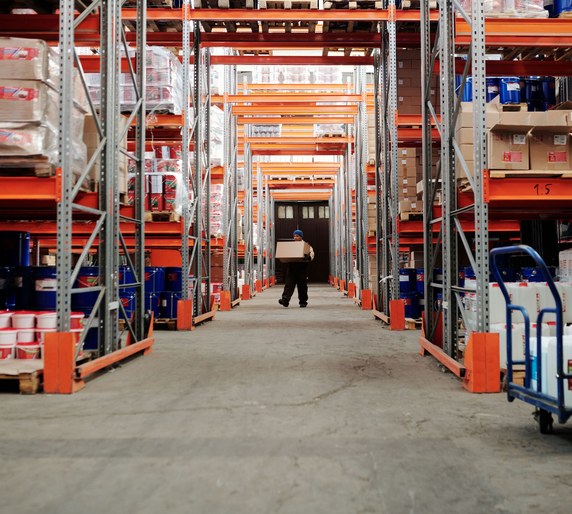 A worker carrying a box down an aisle of tall warehouse racking