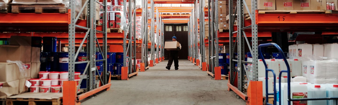 A worker carrying a box down an aisle of tall warehouse racking