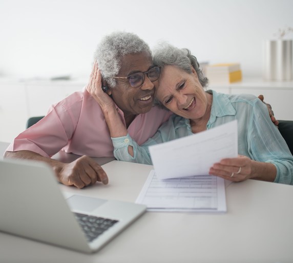 Two people smiling as they read a document together at a laptop