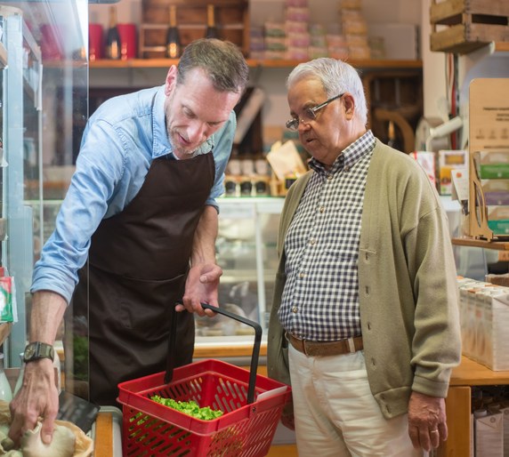 A shop worker in an apron helping an older customer at a grocery counter
