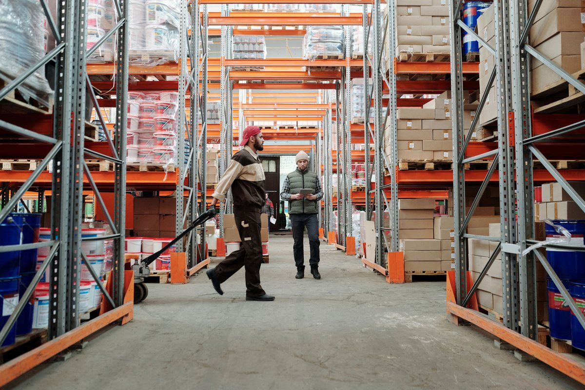 Two warehouse workers moving stock down an aisle of tall racking