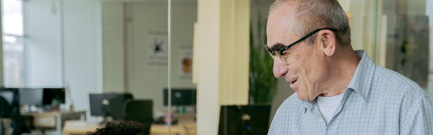 A manager talking with a colleague at a desk in an open office