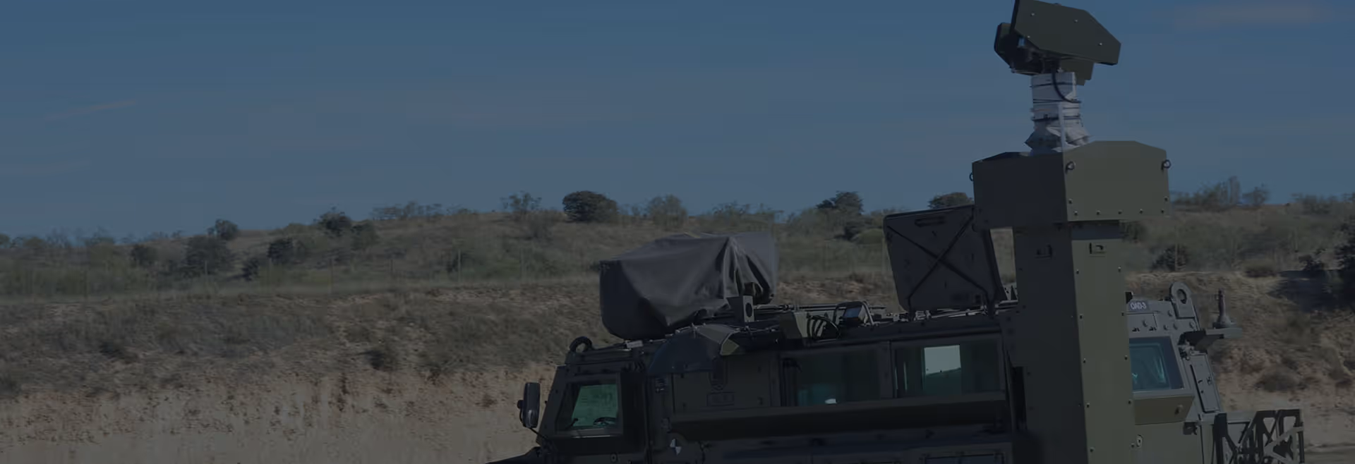 Military vehicle equipped with advanced surveillance or radar equipment under a clear blue sky.