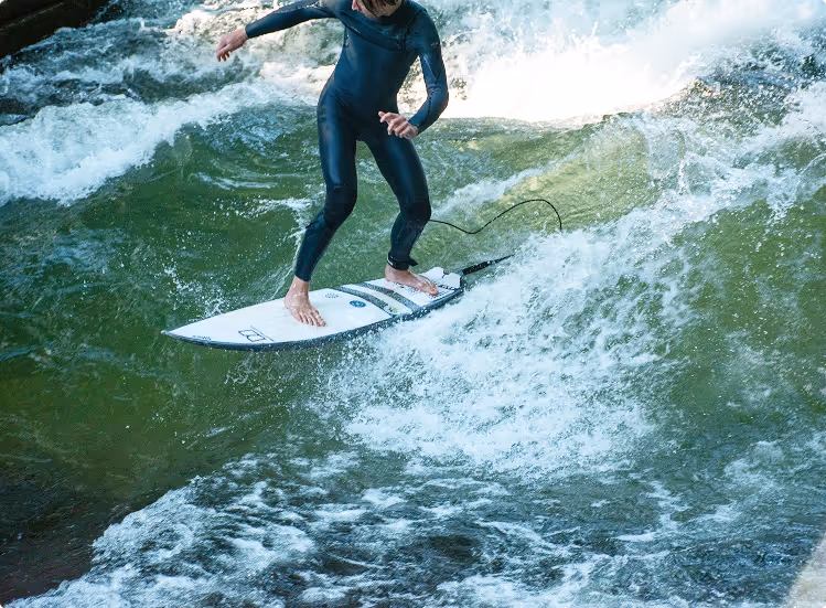 Surfer in einem Neoprenanzug steht auf einem Surfbrett auf einer stehenden Flusswelle mit spritzendem Wasser.
