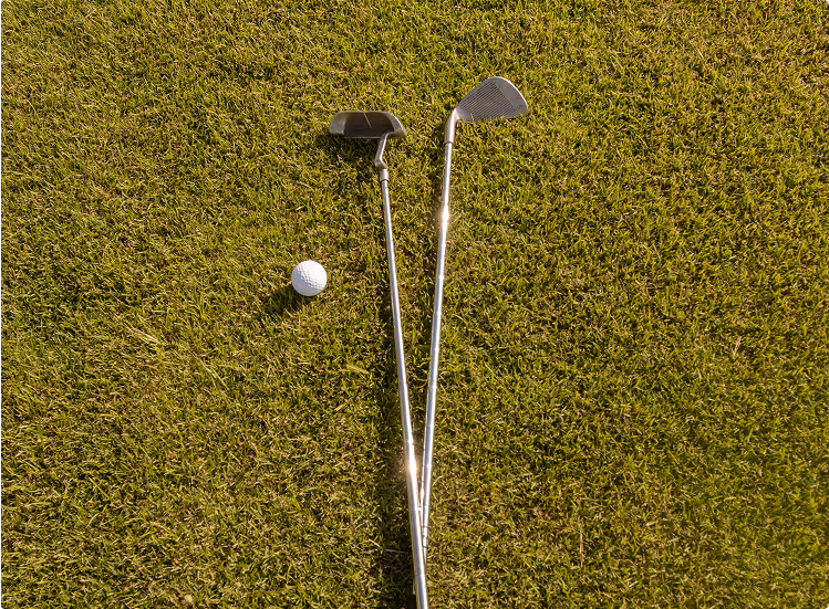 Zwei Golfschläger und ein Golfball liegen auf grünem Gras.