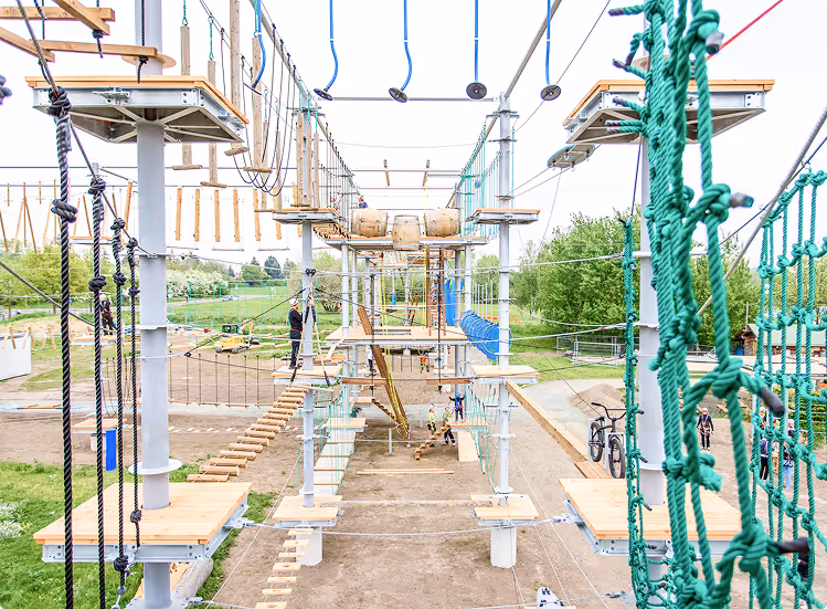 Hochseilgarten mit mehreren Kletteretappen und Menschen, die gesichert verschiedene Hindernisse überwinden.