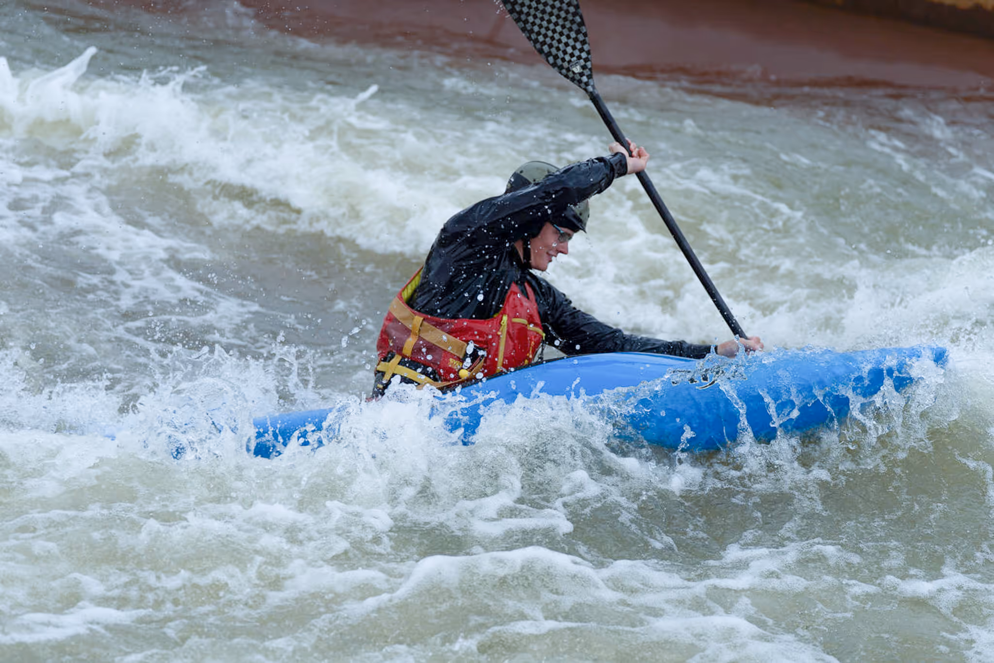 Person beim Wildwasser-Kajakfahren in einem blauen Kajak mit Helm und roter Schwimmweste.