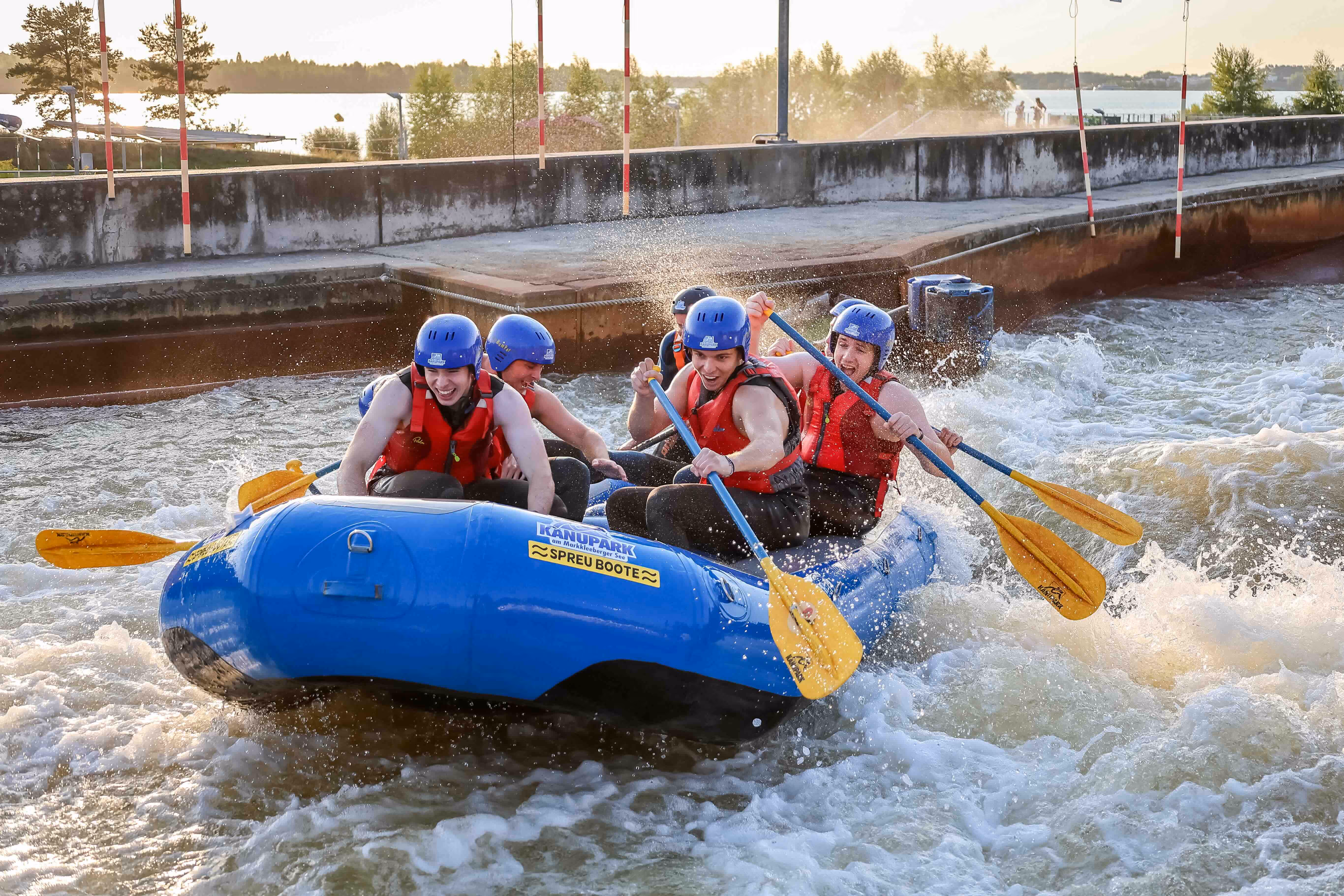 Gruppe von fünf Personen mit blauen Helmen und roten Schwimmwesten bei Wildwasser-Rafting in einem blauen Schlauchboot.