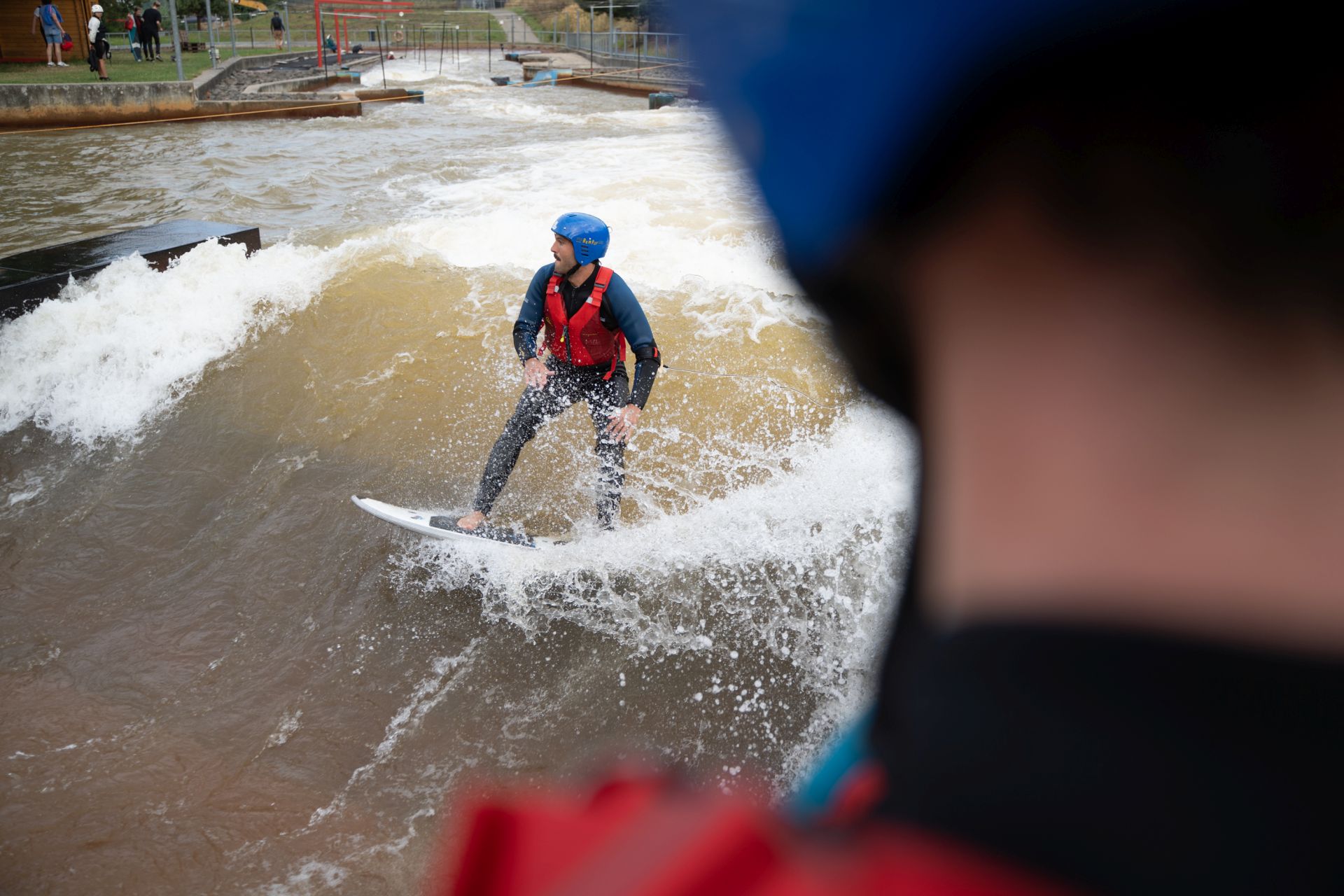 Bild Person in einem Neoprenanzug und Helm surft auf einer stehenden Welle mit einem blauen Bodyboard.