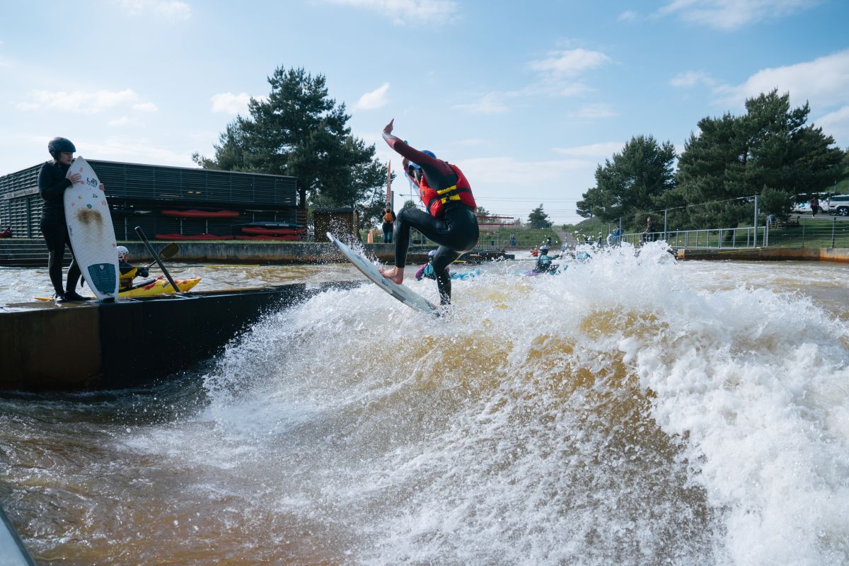 Person in einem Neoprenanzug und Helm surft auf einer stehenden Welle mit einem blauen Bodyboard.