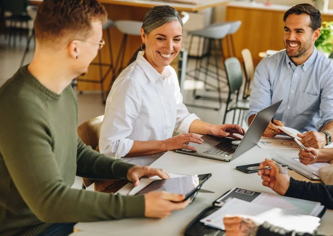 a group of people sitting around a table working on laptops