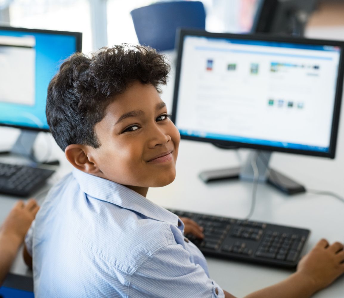 a young male student on a computer looking back over his shoulder at the camera smiling