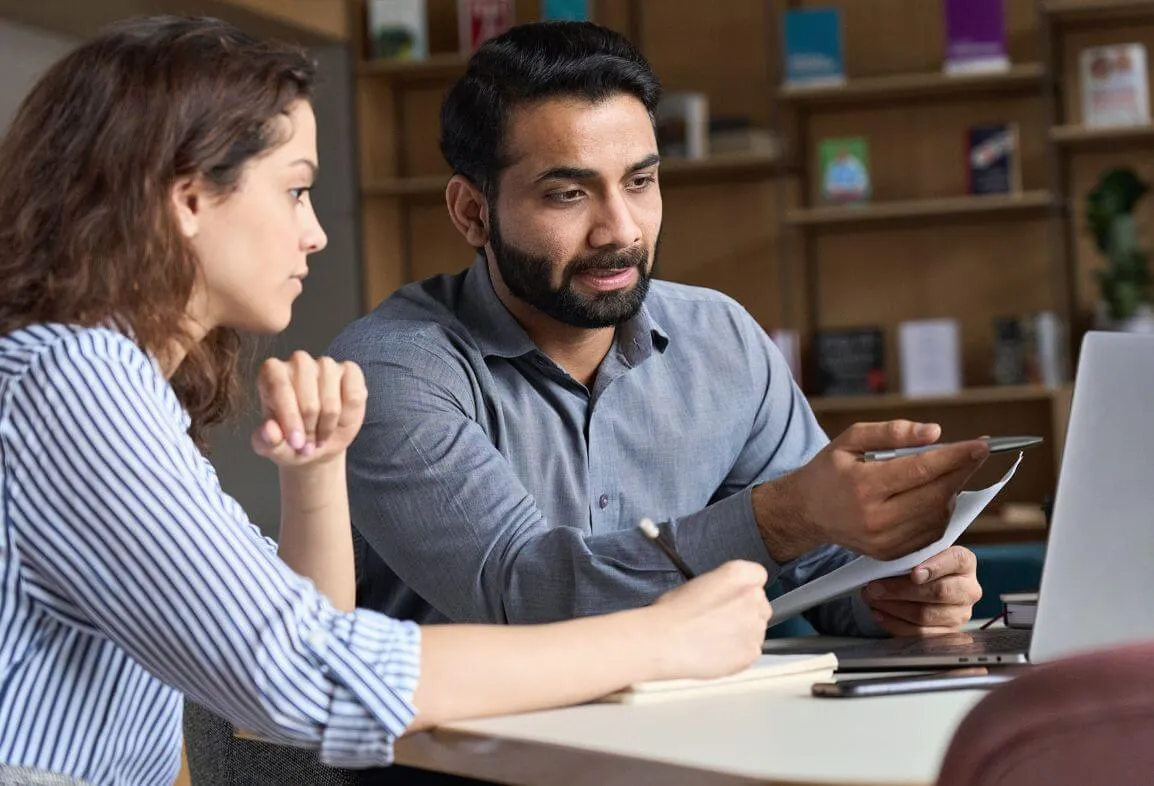 a man and a woman sitting at a table looking at a laptop