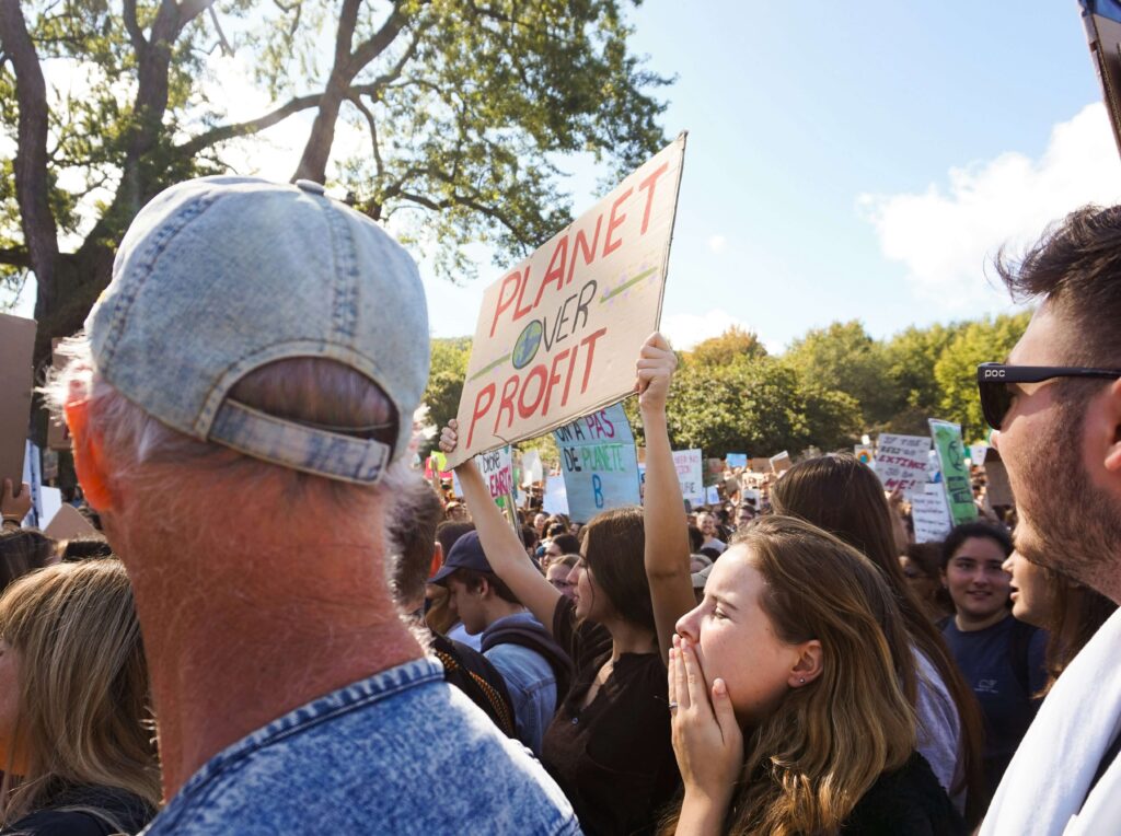 Group of individuals protesting climate change. A woman in the middle of the group is holding up a sign that reads "Planet over Profit."