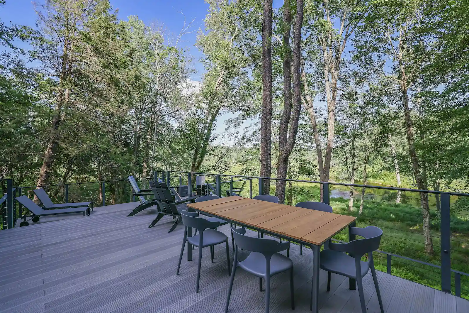 Outdoor wood deck with a dining table and lounge chairs surrounded by tall trees at Camp Double Oak