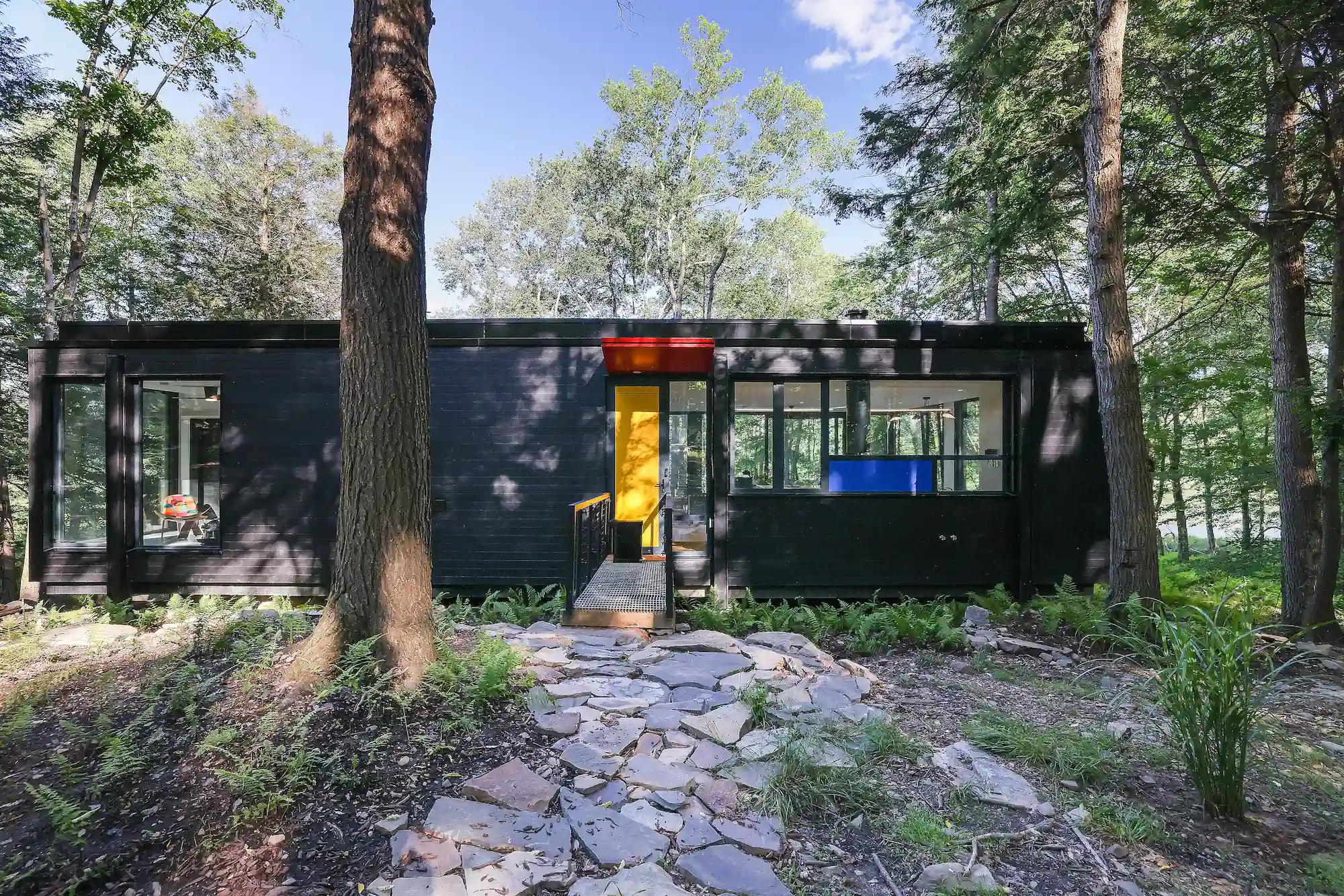 Exterior of Camp Double Oak's black modern home with a yellow front door and stone pathway through the trees