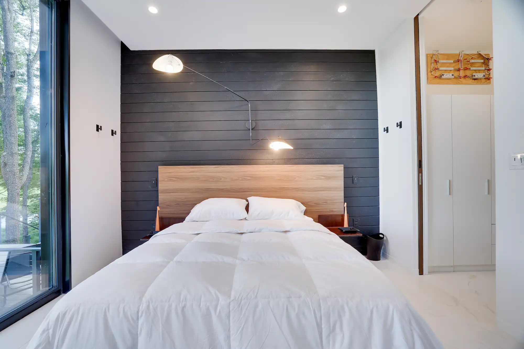 Bed with a walnut headboard against a charred wood accent wall and sconce lighting.