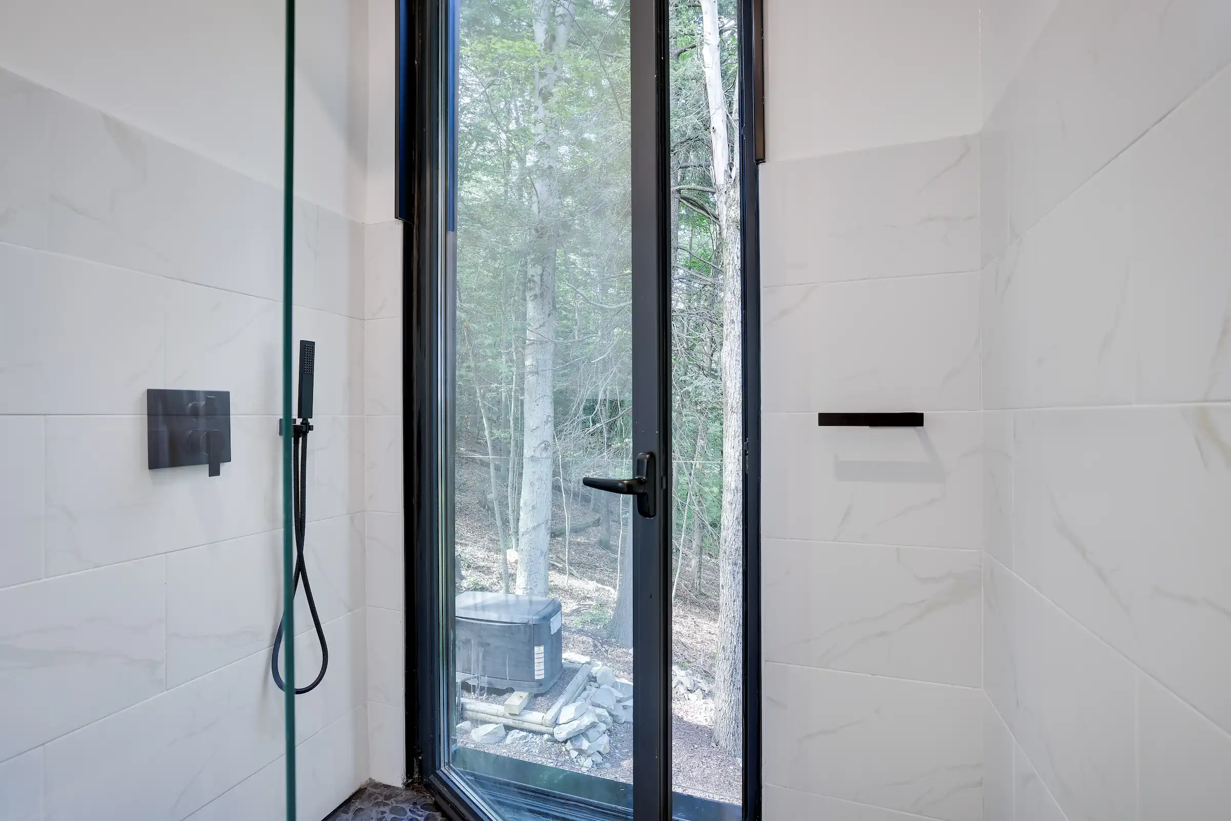 Walk-in shower with a glass door opening directly to a private outdoor shower deck in the woods.