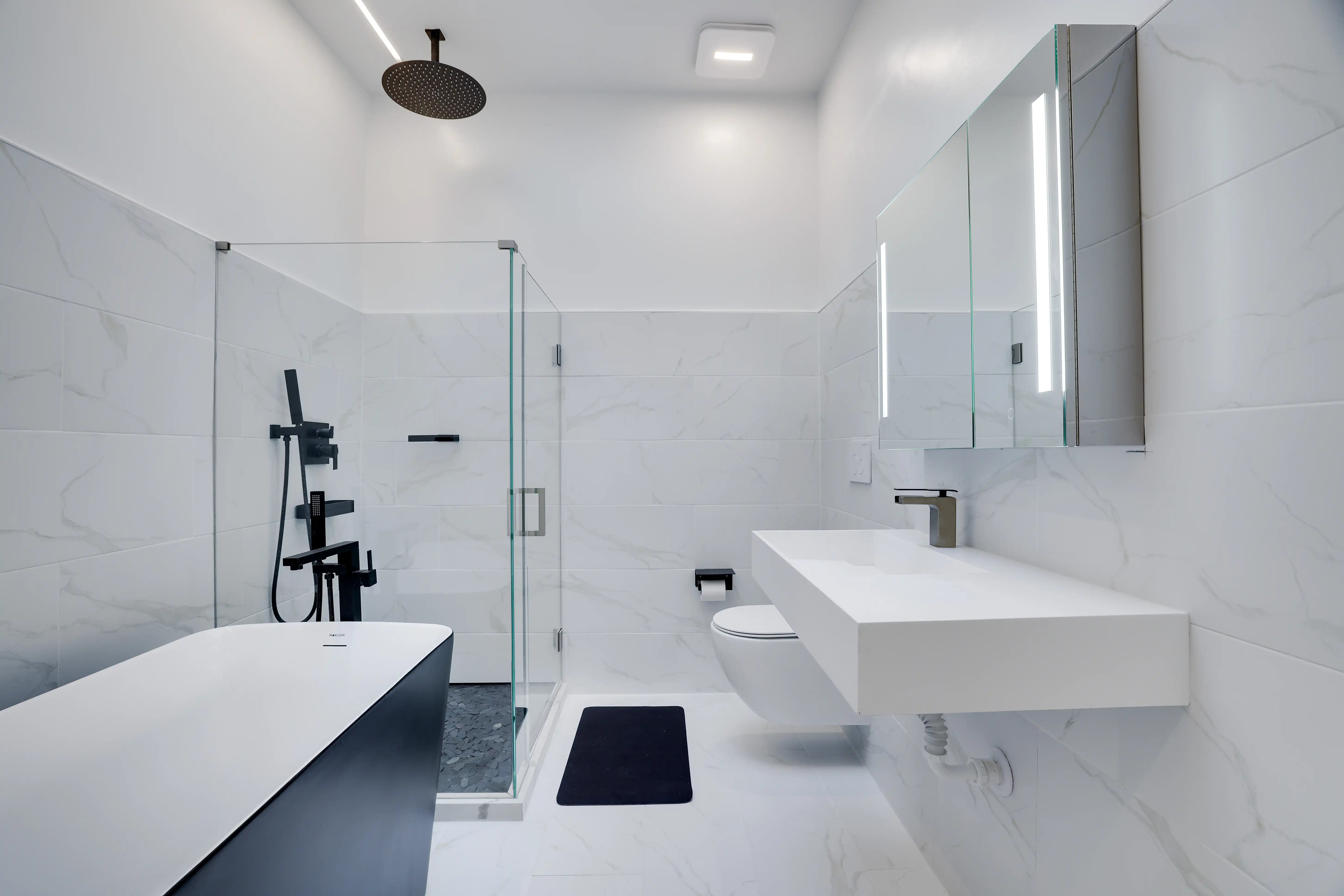 Bathroom with glass rain shower, floating vanity, and freestanding tub in white marble tile.