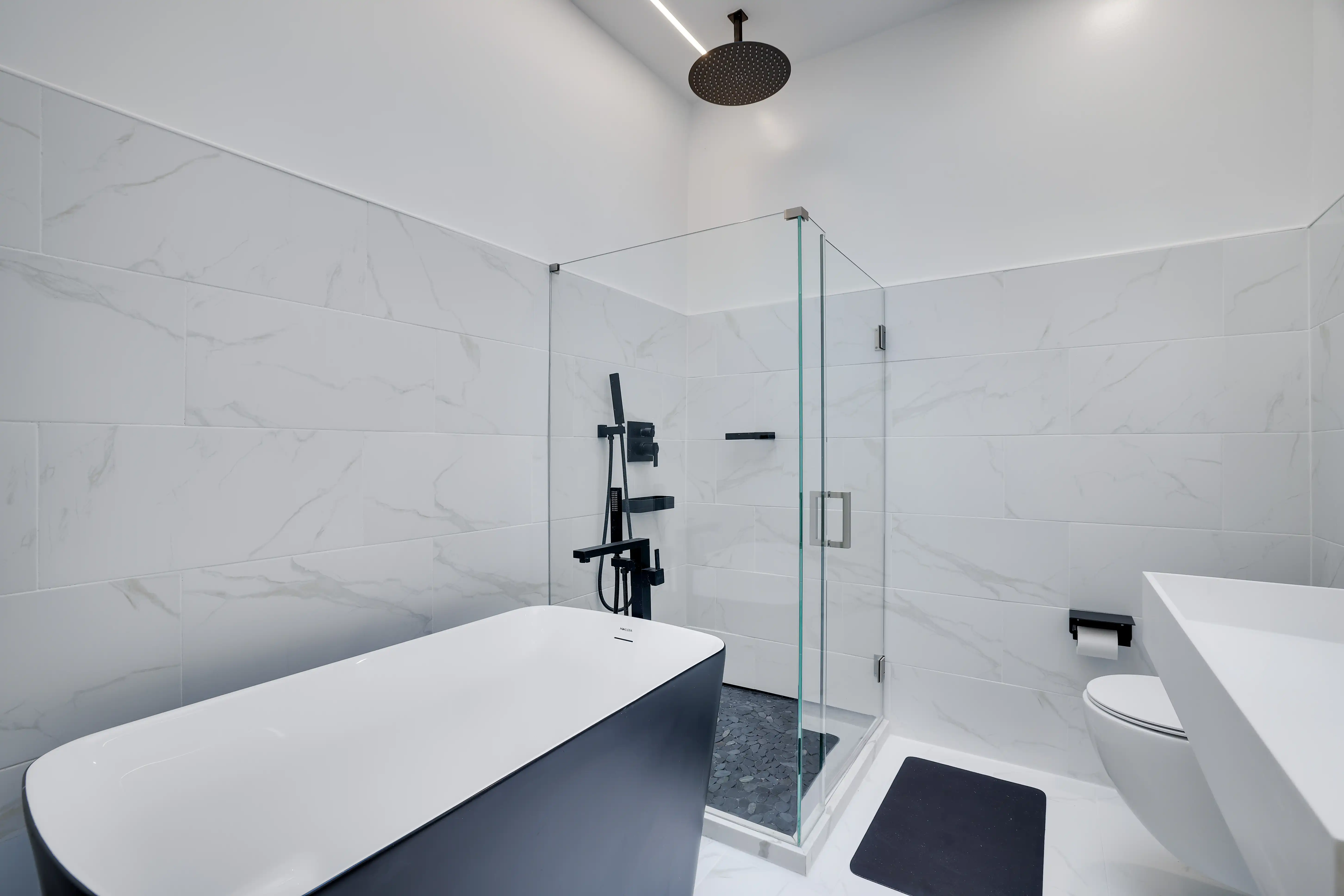 Freestanding soaking tub beside a glass-enclosed rain shower in a marble-tiled bathroom.