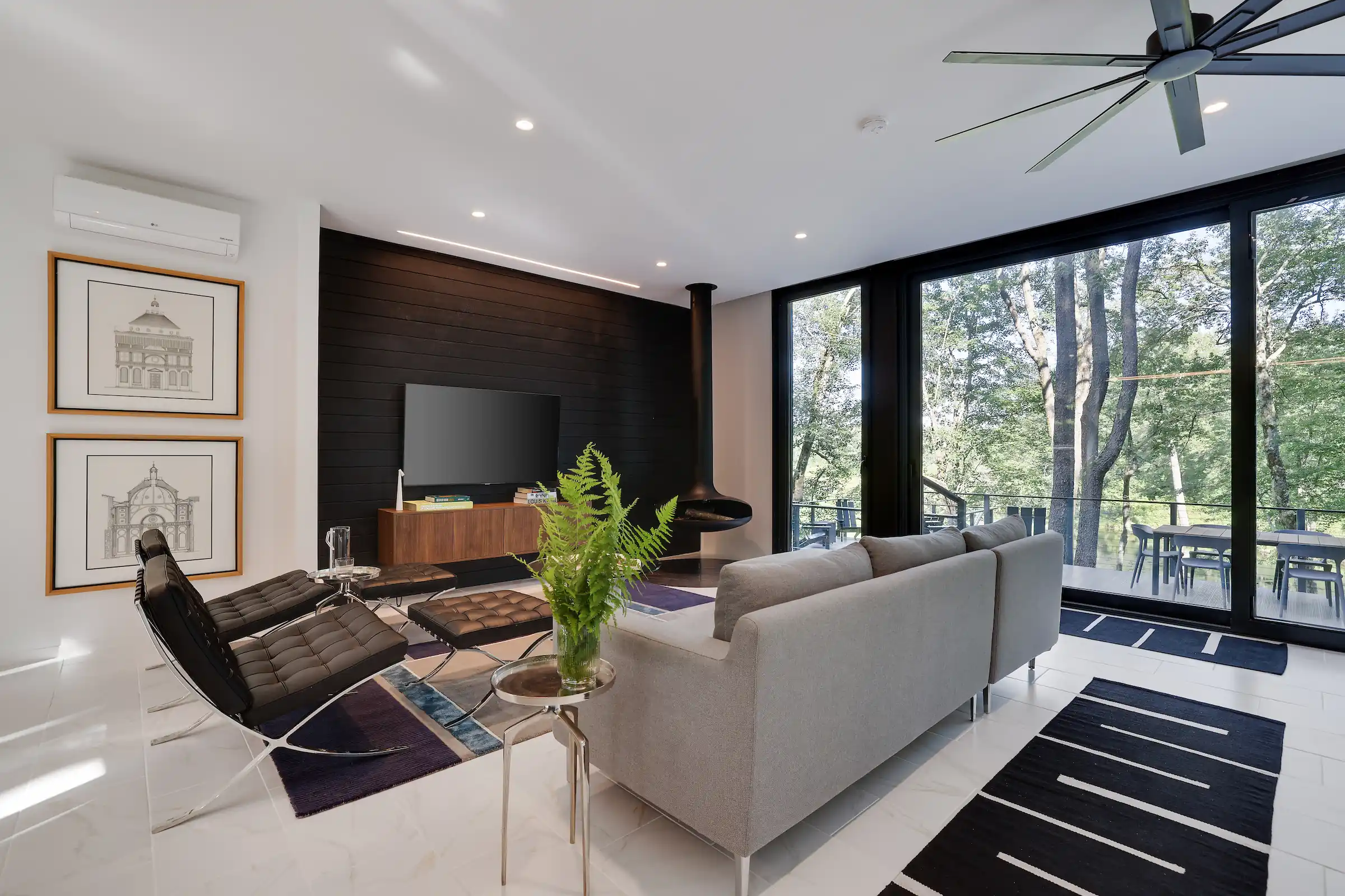 Living room with Barcelona-style leather chairs, a glass coffee table, and floor-to-ceiling windows framing the surrounding trees.