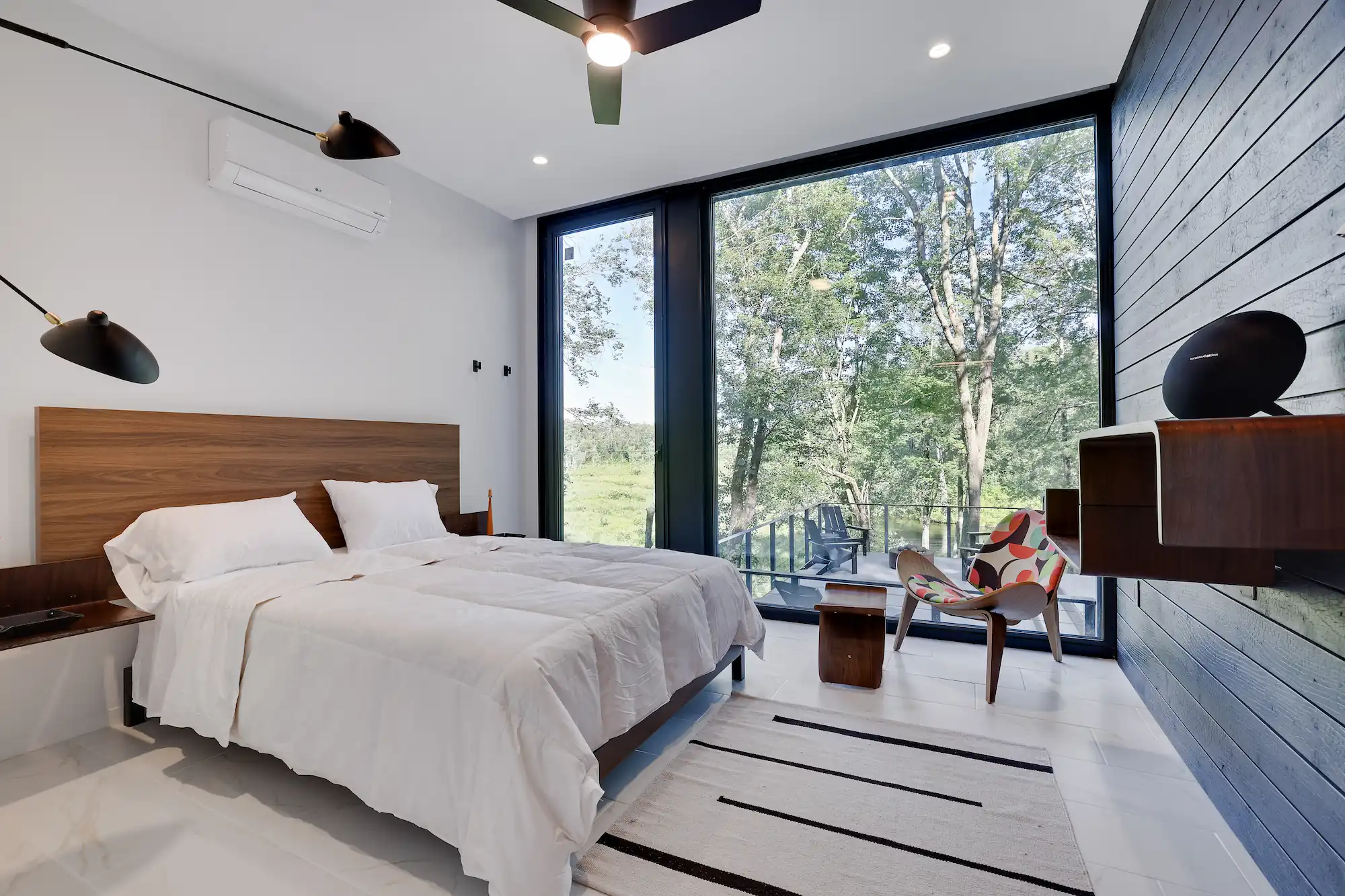 Walnut-headboard bed facing floor-to-ceiling glass with forest views and a private deck.