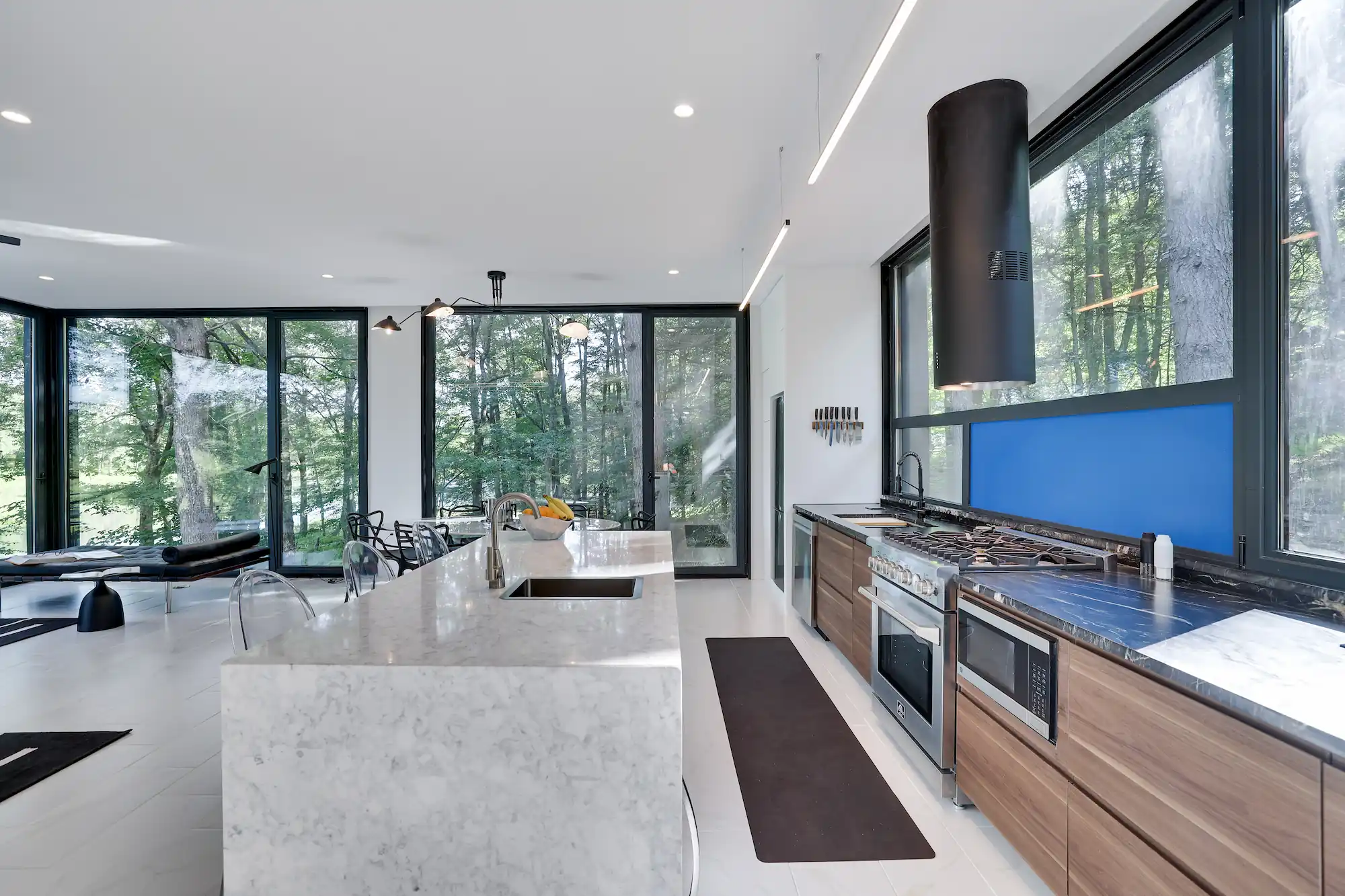 Kitchen with marble island and stainless range framed by floor-to-ceiling windows overlooking the trees.