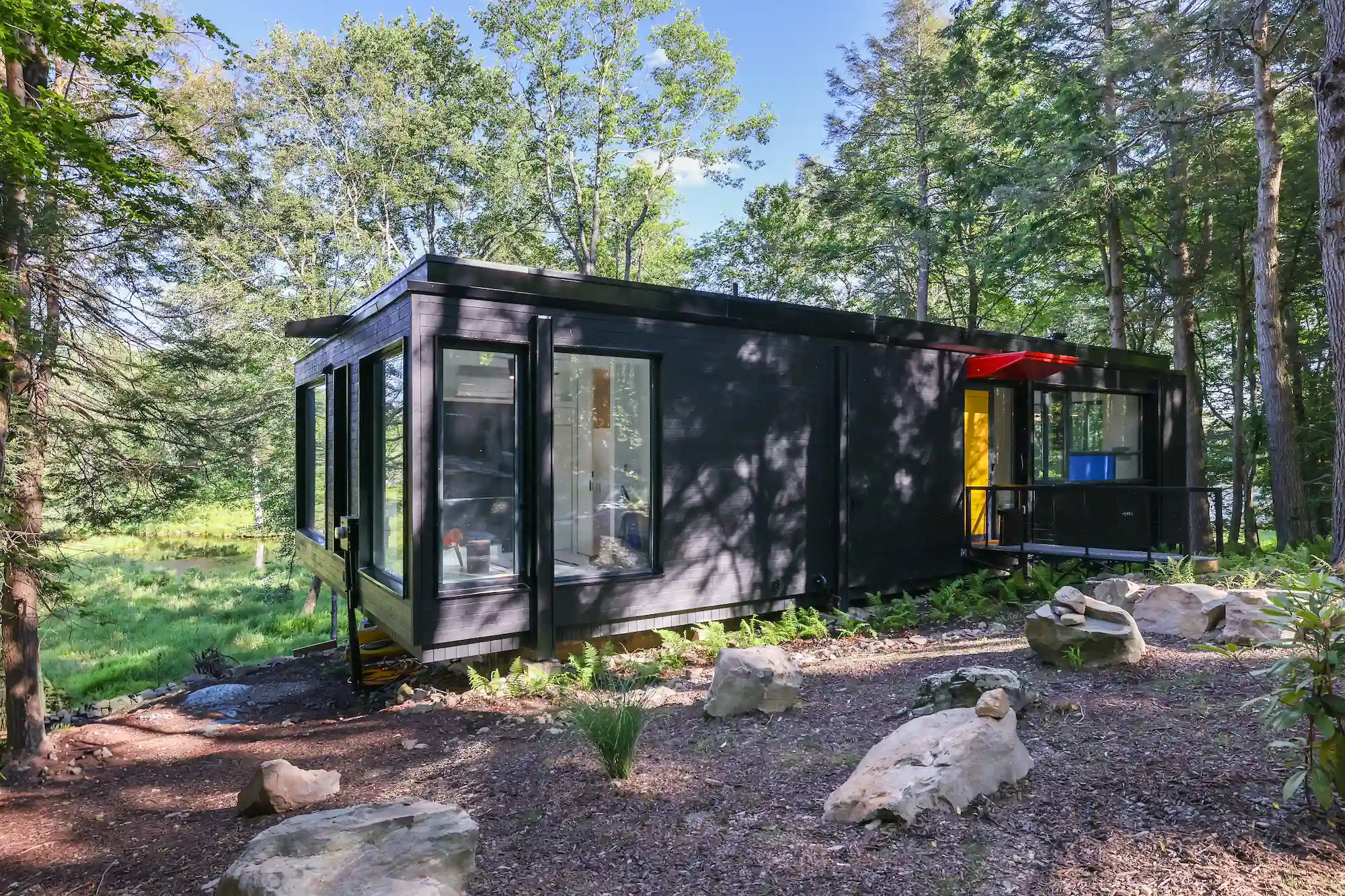 Black charred-wood exterior of Camp Double Oak nestled among trees, with a covered deck entrance.