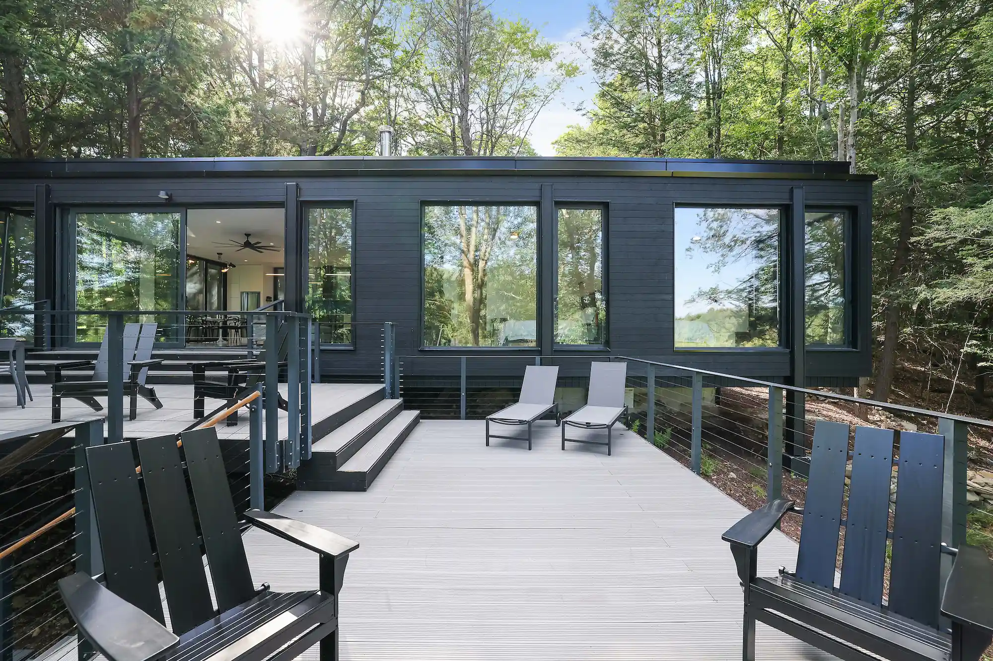Elevated wraparound deck with Adirondack chairs and loungers set against the glass exterior of the cabin.
