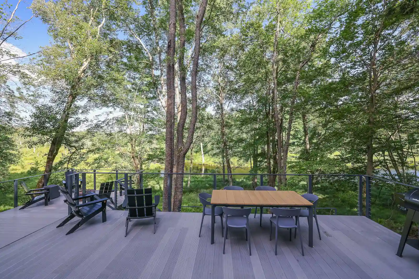 Outdoor dining table and Adirondack chairs on the deck overlooking the forest and private lake.