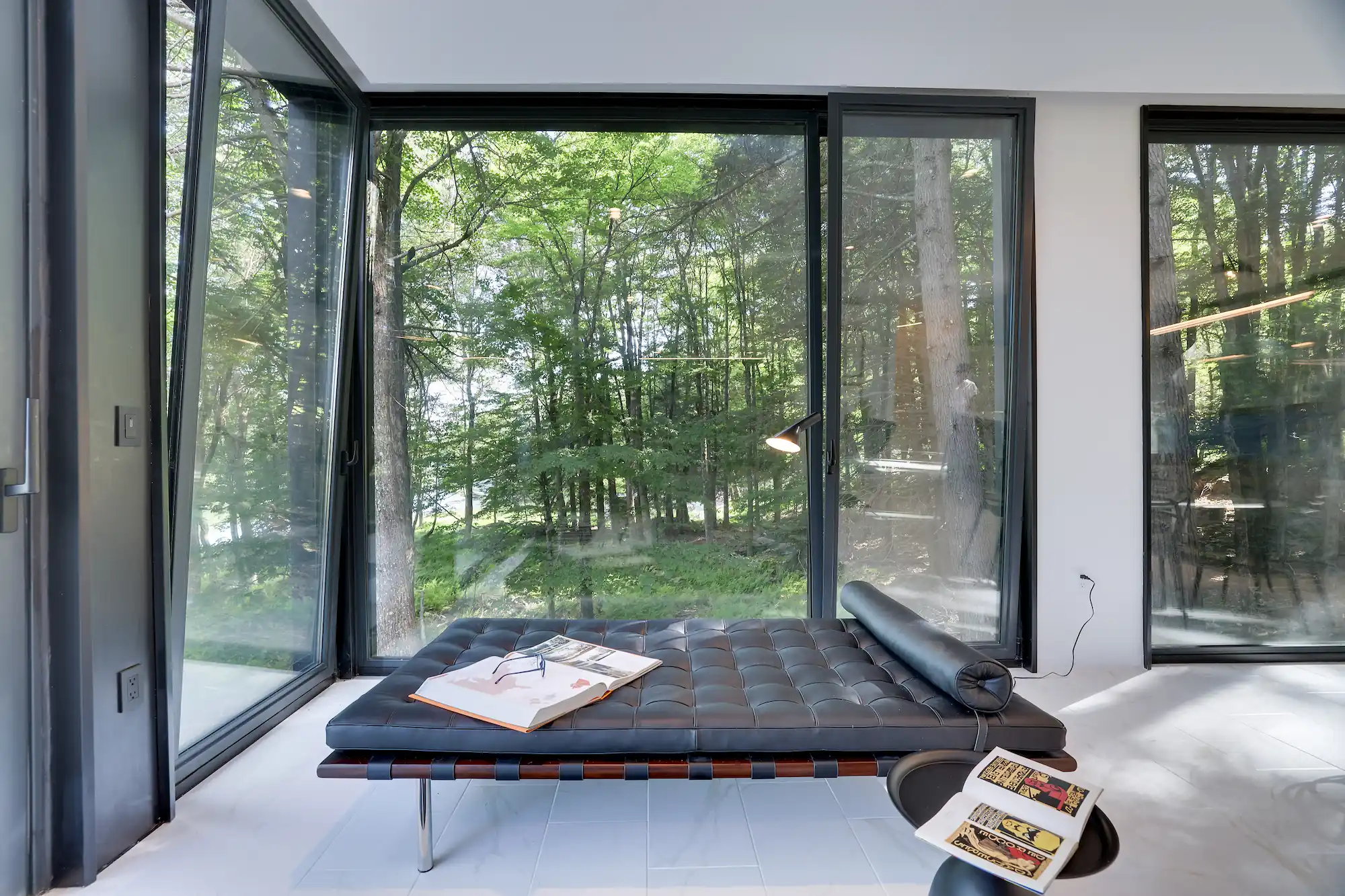 Barcelona daybed positioned at a glass corner overlooking the private lake through the trees.
