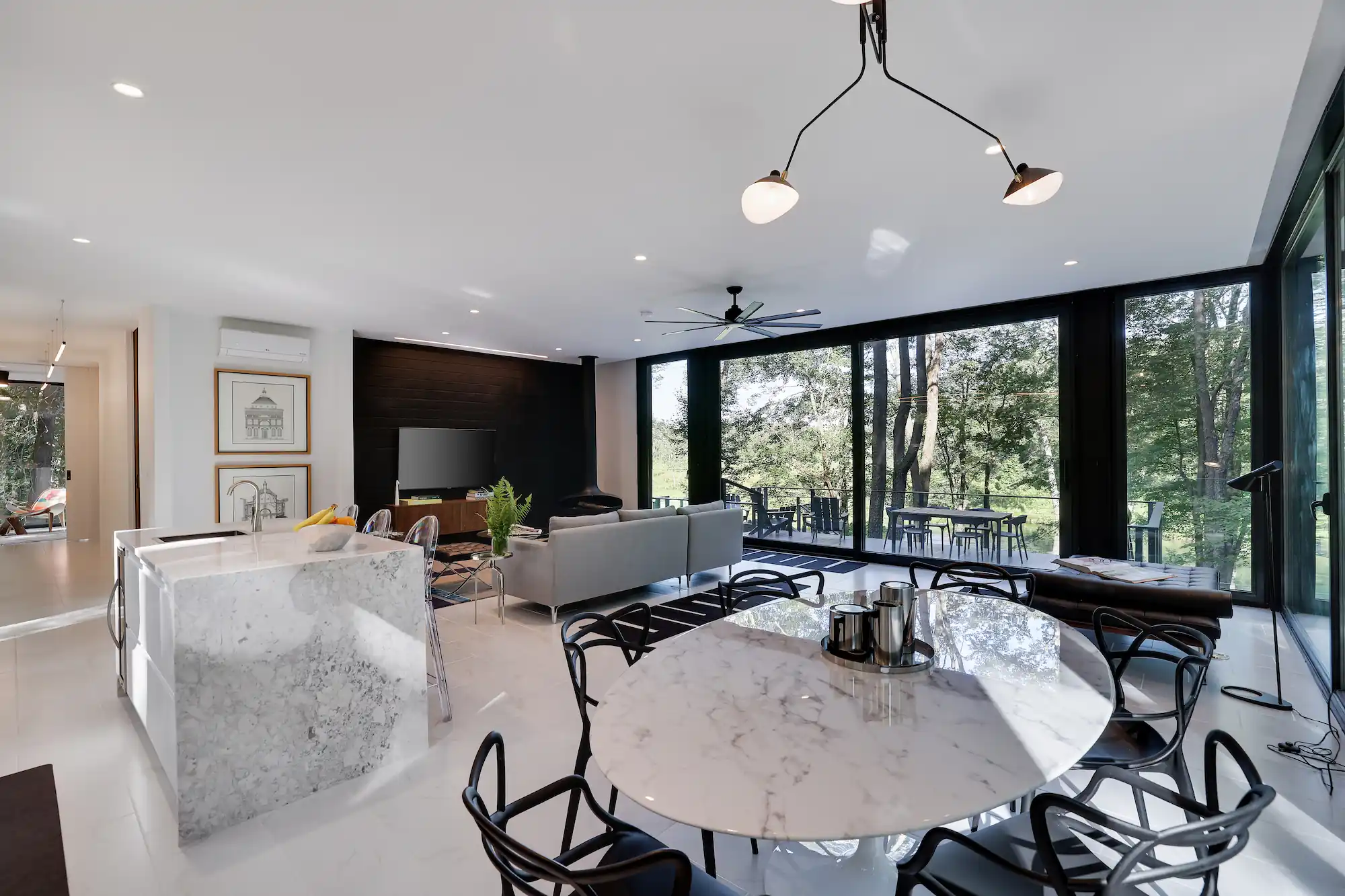 Waterfall marble kitchen island beside a round dining table, framed by glass walls overlooking the woods.