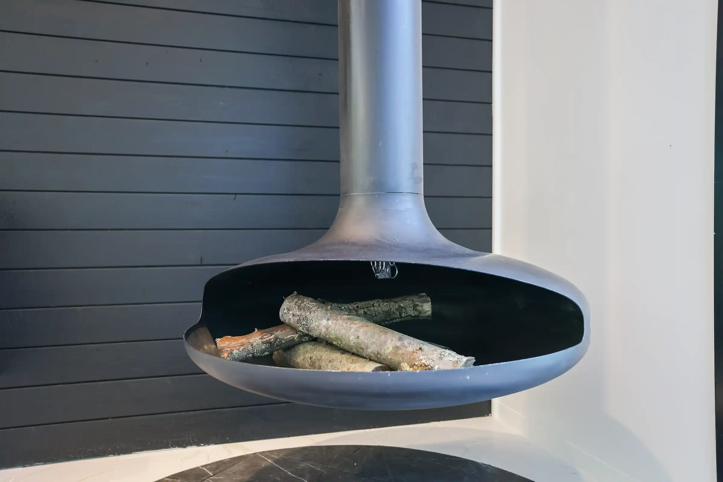Close-up of the suspended fireplace loaded with firewood against a charred wood accent wall.